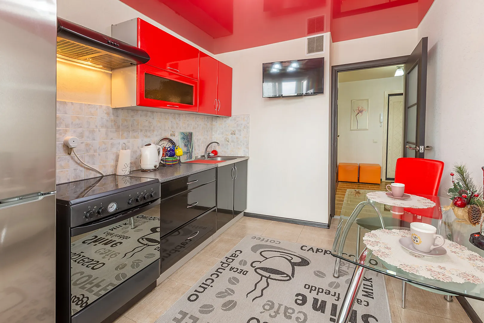 Просторная кухня с кухонными принадлежностями, с телевизором и большим холодильником.