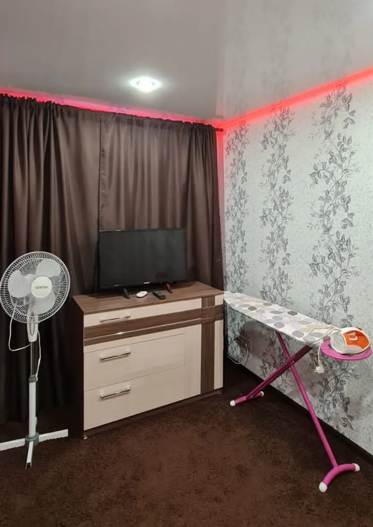 В спальне телевизор, вентилятор и гладильная доска с утюгом.