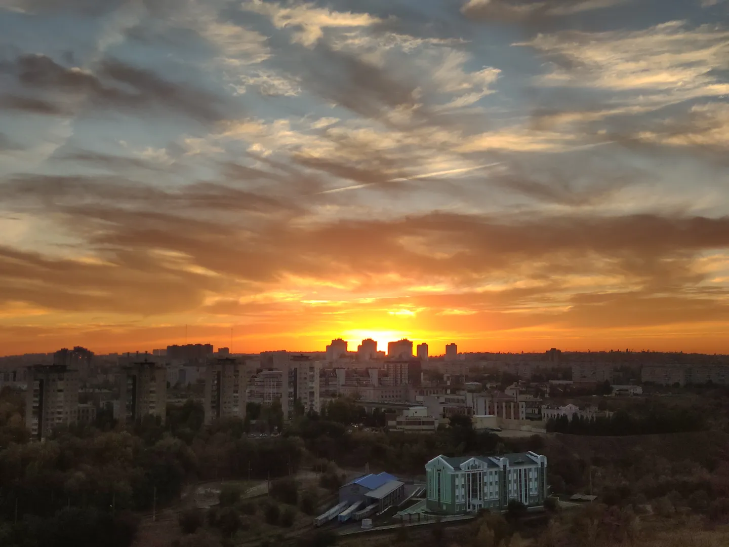 Закат солнца.  Всегда живая картина города в окнах. На переднем плане вокзал Детской железной дороги.