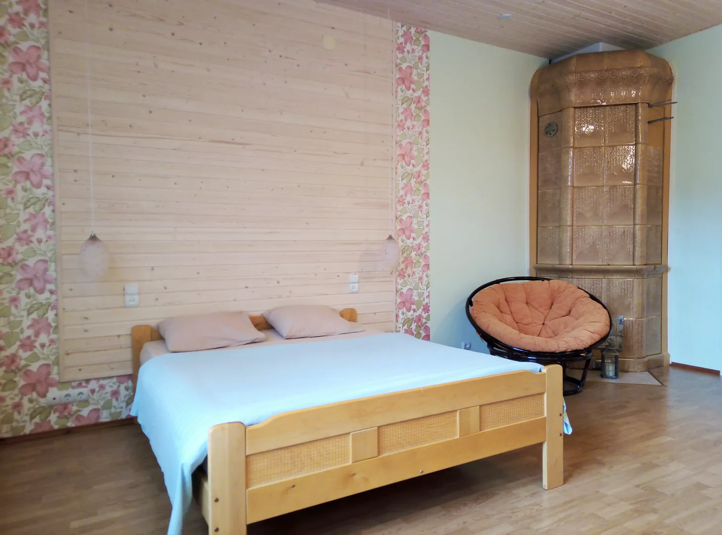 Удобная широкая двуспальная кровать из массива березы и уютное ротанговое кресло у финской изразцовой печи
