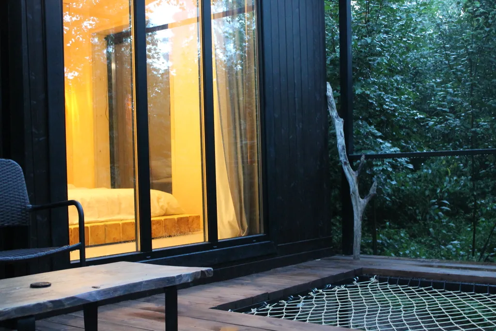 Дом с ванной у панорамных окон и высокой террасой в лесу