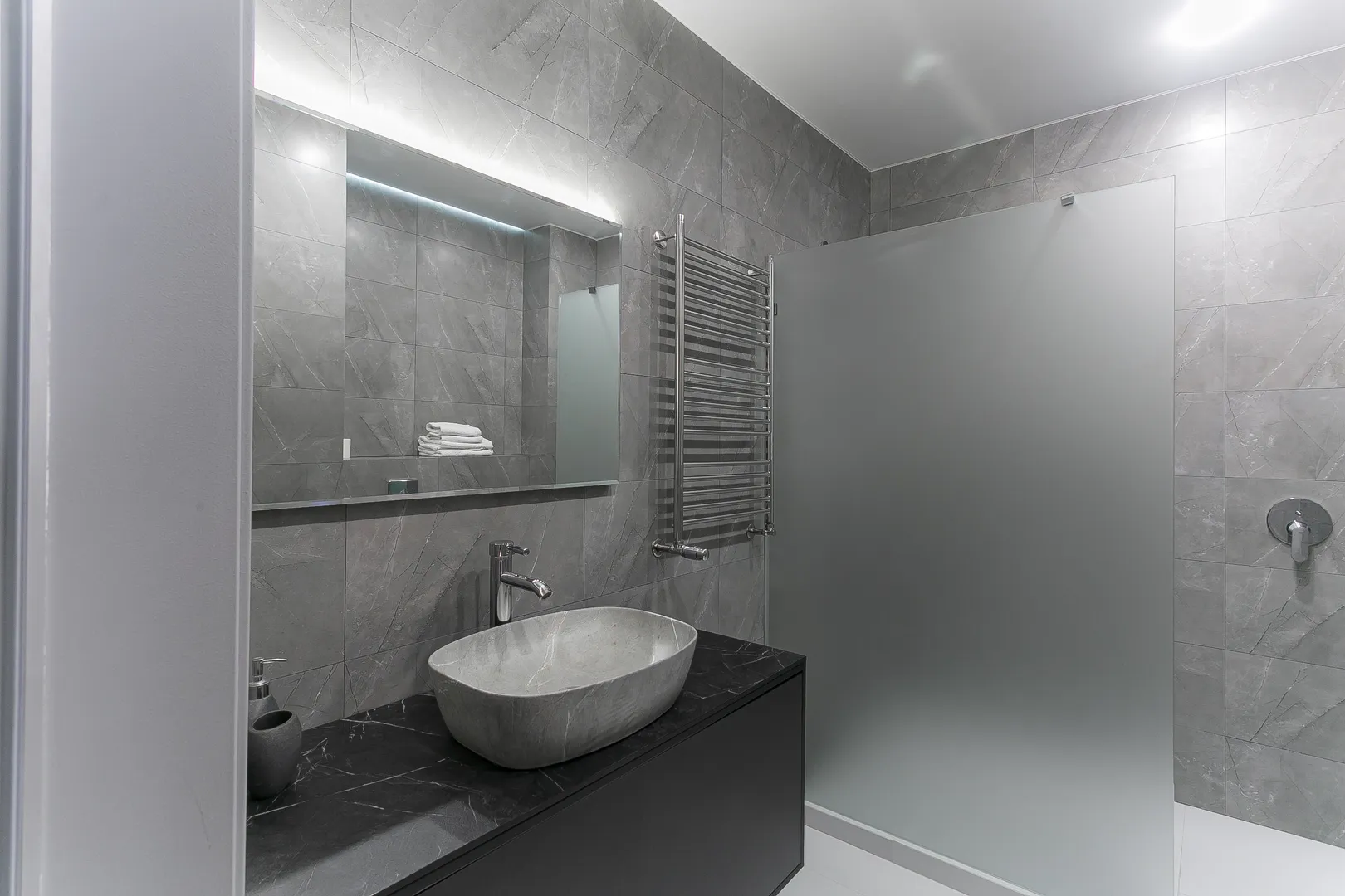 Ванная комната оборудована встроенным унитазом, гигиеническим душем, раковиной, тумбой с выдвижными ящиками, просторным душем, полотенцесушителем, зеркалом с подсветкой