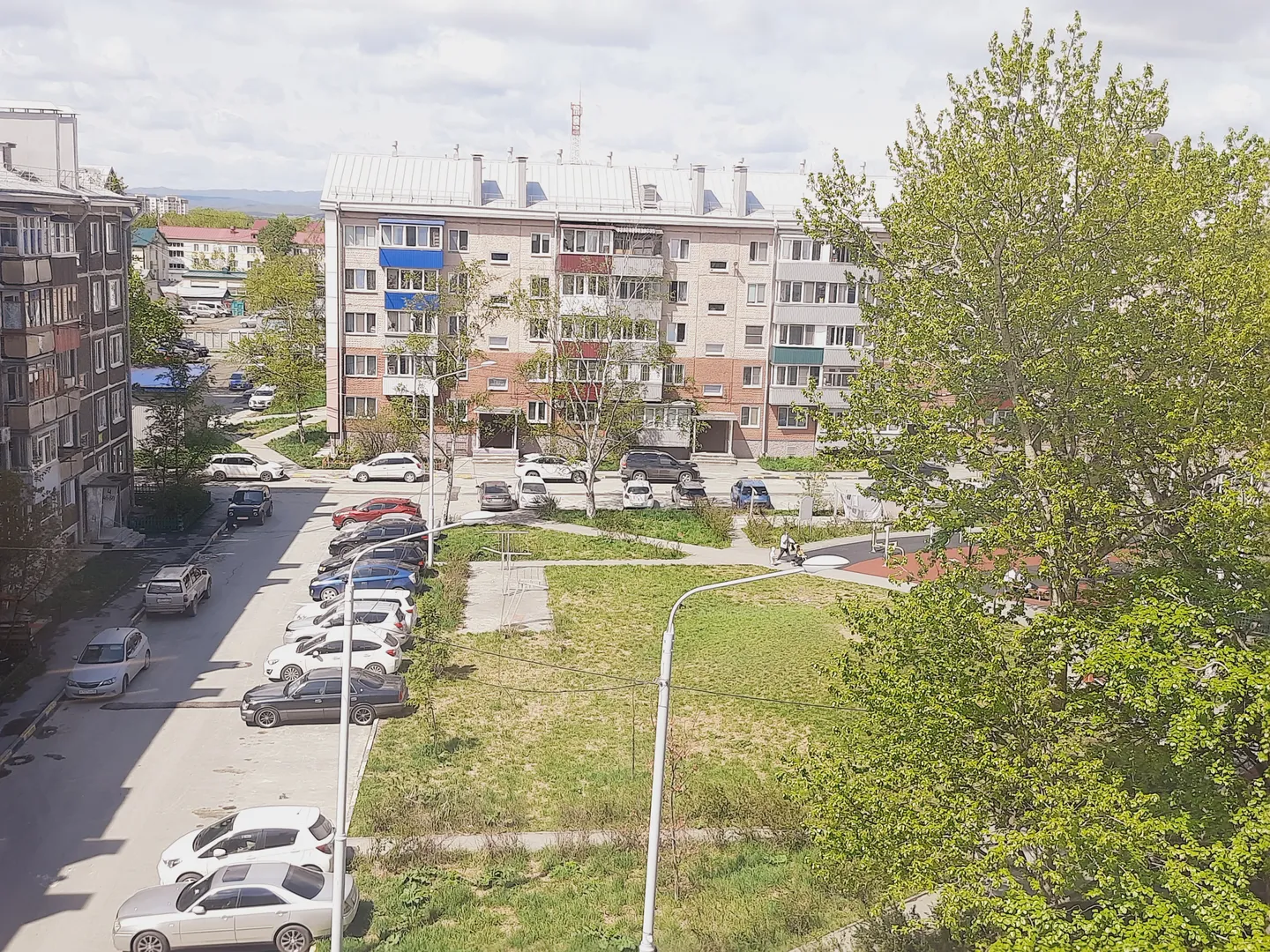 Вид с балкона, гостиной, кухни: зелёный двор, немного поодаль детская площадка, на горизонте - сопки, Мицульский хребет.