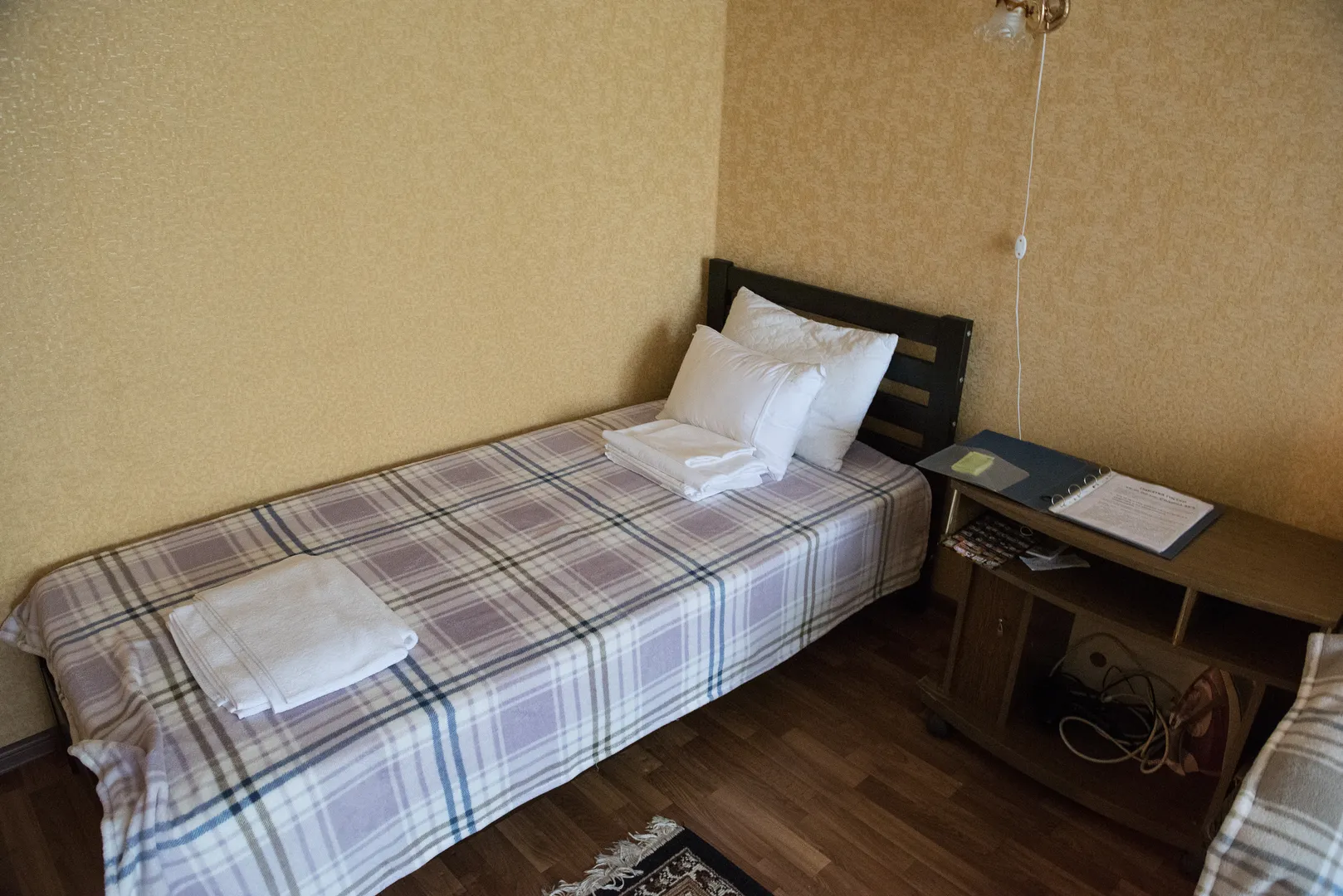 Спальня: односпальная кровать в деталях, прикроватная тумбочка с утюгом и памяткой для гостей